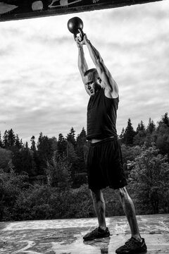 White man lifting kettlebell overhead during outdoor workout
