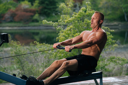 White man rowing on exercise machine outdoors by lake