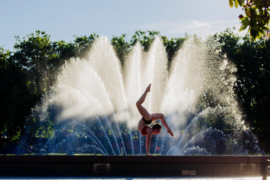 Handstand acrobat balancing in front of water fountain in outdoor park