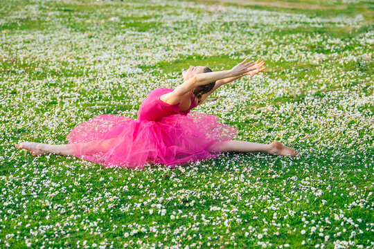 Ballet white dancer stretching in split on daisy field outdoors