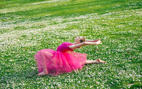 Ballet white dancer in pink tutu stretching in daisy field outdoors