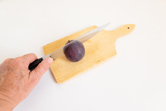 hand cutting a fresh purple fig with a knife on a cutting board