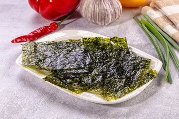 Crispy nori seaweed sheets on white plate with red pepper, garlic, and green onions in soft natural light © Andrei Starostin