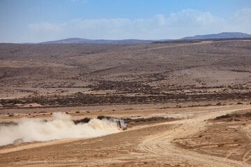 Off-road SUV driving across desert plain trailing a cloud of dust © mstudio