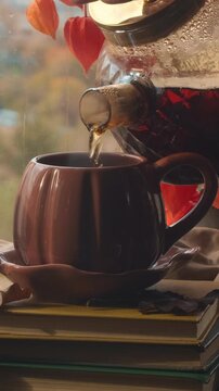 Vertical video. Autumn mood. Pouring tea into mug from teapot. Cup of hot drink near window. Drinking tea in cozy atmosphere indoors