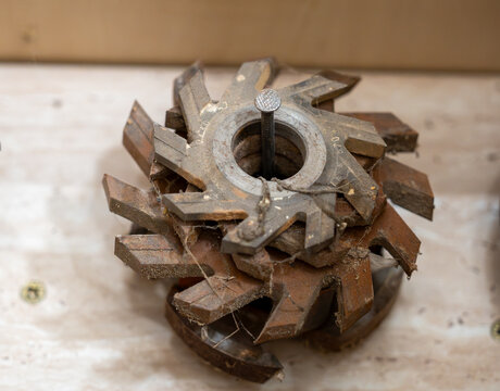 Close-up of stacked used woodworking milling cutters with sharp cutting edges, rust and sawdust, showing professional router tooling stored in a carpentry workshop.

