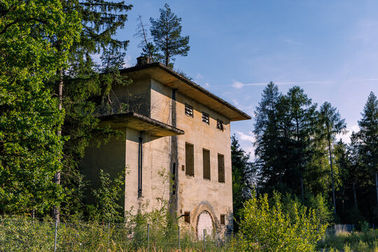Abandoned old concrete building and ruin surrounded by green forest trees, lost place and nature taking back architecture concept