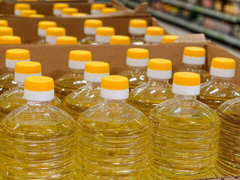 Yellow vegetable oil in plastic bottles stands within cardboard boxes on grocery store counters, depicting sunflower oil packaging and organized product placement