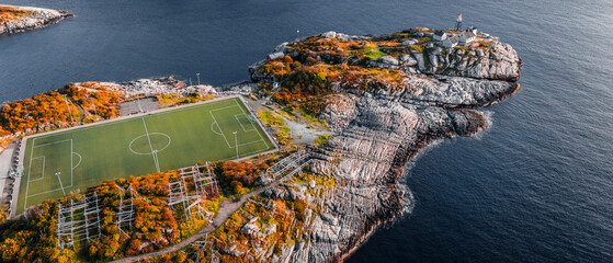 High angle aerial drone view of the famous Henningsvaer football field and lighthouse on rocky coast surrounded by ocean water in Lofoten Norway © Quality by Simon