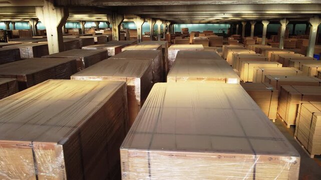 Rows of stacked wooden plywood boards and MDF panels packed in plastic wrap in large industrial warehouse   