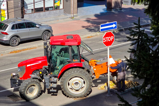 Ukraine. Khmelnytskyi. September 16, 2026. A red tractor with a hydraulic earth auger attachment drilling a hole in a city sidewalk next to road signs.