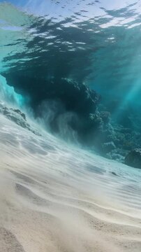 Vertical video: Rippled seabed releasing rising sand plumes after swell at reef, sunlit shafts