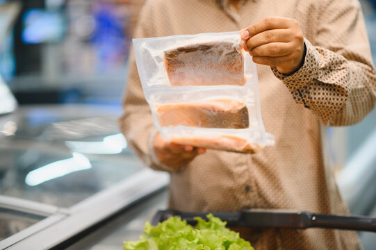 Shopper holding packaged frozen salmon fillets in supermarket