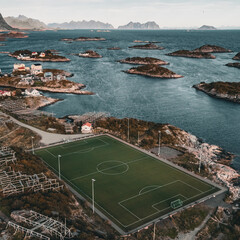 Vertical aerial drone view of the iconic Henningsvaer football field on a rocky island with scenic fjord and mountains in Lofoten Norway © Quality by Simon