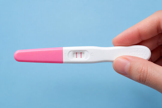 A pink and white ovulation predictor kit is being held by a person's hand against a light blue background.