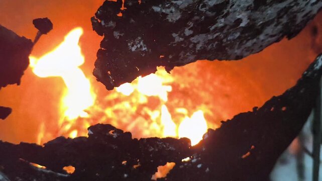 Close-up of an active fire producing bright flames and glowing embers, capturing the intense heat, natural combustion process, smoke, and warm textures of burning material.