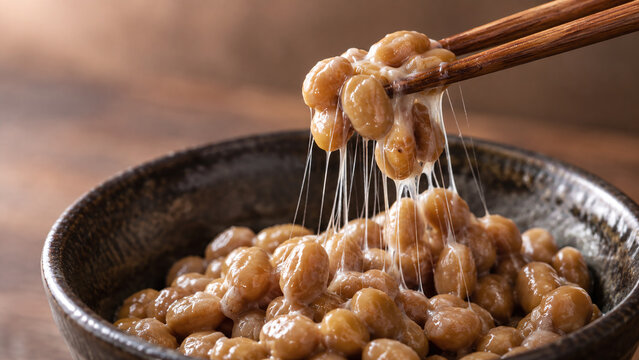 Chopsticks lifting sticky natto fermented soybeans from a ceramic bowl