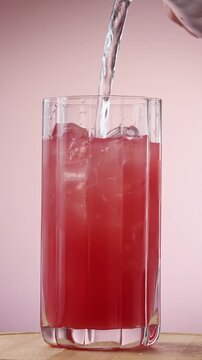 Clear mixer tops rotating tall watermelon drink with ice in clear glass on pink studio background.