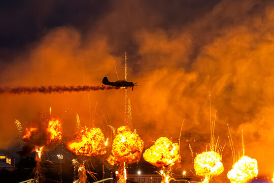 Bucharest, Romania Propeller airplane of Iacarii Acrobati performs at BIAS over spectacular fire explosions and pyrotechnic wall of flame during an impressive night aviation airshow.