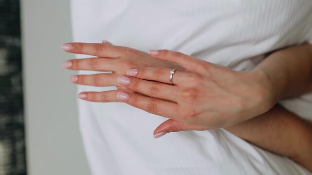 The woman is lying on the bed and gently runs her fingers over her arm. She barely touches herself.