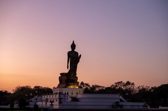 Stand big Buddha Statue silhouette during sunset Light background in park of Thailand temple. Yellow light silhouette dark shadow of image Buddha statue stand Buddha tall walk sun light cloud.