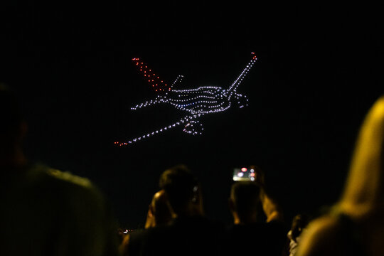 Bucharest, Romania Luminous airplane shaped drone show lighting up the dark night sky at BIAS aviation event with audience filming the futuristic aerial light performance spectacle.