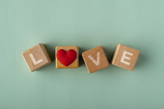 Wooden blocks spelling the word LOVE with a red heart icon replacing the letter O on a light green background. Top view flat lay photography, copy space.