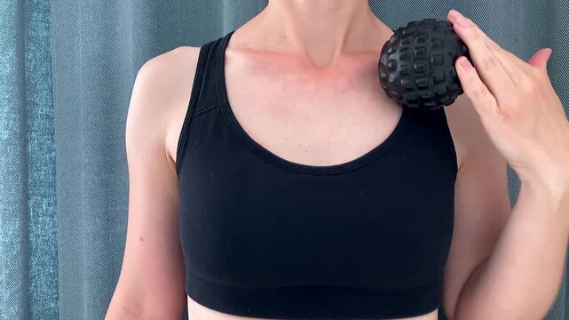 A woman uses a black massage ball at home to target specific muscles in the body, relax after a workout, and maintain good blood circulation. Close-up