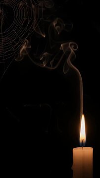 Glowing Candle and Spiderweb in Darkness - A single white candle burns brightly, its flame casting a warm glow against a dark background.