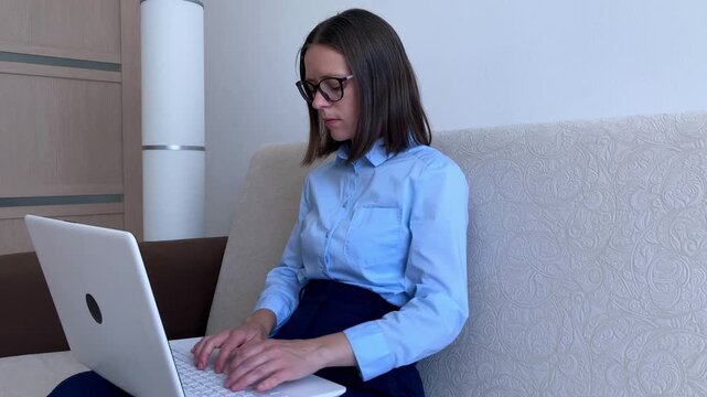 A young woman with short hair and glasses is sitting on a sofa and typing on a laptop, interacting with AI in a home environment. The topic of using neural networks and digital tools in everyday work