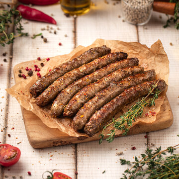 Juicy roasted grilled sausages served on parchment paper on wooden cutting board with herbs and spices