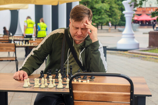 Adult man sitting at an outdoor chessboard park, deeply thinking and strategizing his next move in a classic intellectual board game.