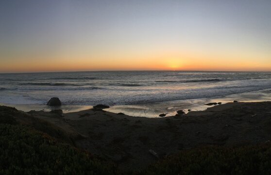 Wide angle view of the sun disappearing on the ocean horizon during sunset in San Simeon, California.
