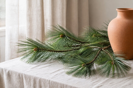 Longleaf pine branches with terracotta urn on linen cloth, natural decor concept