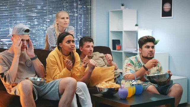 Eight adults sitting on a sofa in a modern living room, reacting with disappointment while watching an unseen event during daytime leisure time.