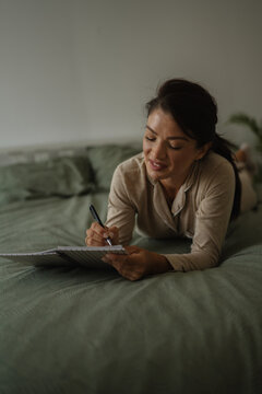 Woman writing in journal on bed for reflection and leisure