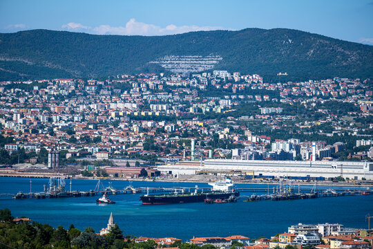 Muggia, Italy - August 8, 2026: Panoramic view of the Gulf of Trieste and the industrial port area with tankers and the city cityscape on the hills.