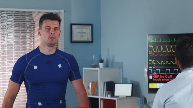 Two middle-aged men in a medical clinic: an athlete in blue sportswear faces forward while a doctor in a white coat reviews data on a medical monitor and tablet.