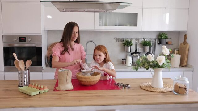 Mother and daughter sifting flour while baking cookies