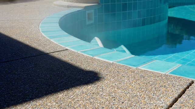 Tranquil outdoor swimming pool scene with turquoise tiles and shimmering water, capturing a sunny summer day.