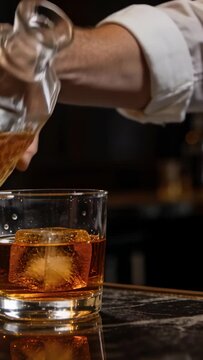 Vertical video: Lifting jigger at bar man in rolled sleeve pouring spirit into glass ice to serve