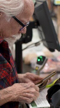 Pays at the checkout for fresh vegetables and food while shopping in a grocery store. He interacts with the checkout process.