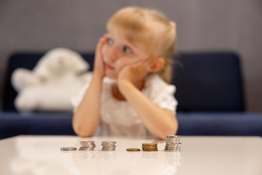 A preschool-aged girl is counting coins on the living room table. The child is frightened there isn't enough money; she is surrounded by poverty and a lack of resources 