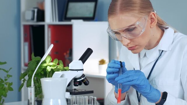 Female scientist wearing safety glasses and gloves carefully transferring sample with pipette in an indoor laboratory research facility.