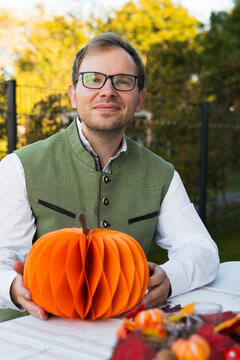 Man sitting at an autumn table and holding a paper pumpkin, illustrating autumn spirit with warm seasonal colors.