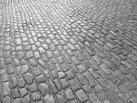 A detailed black and white high angle texture of an old historic cobblestone street road, showcasing uneven vintage stone blocks patterned for a rustic urban background.