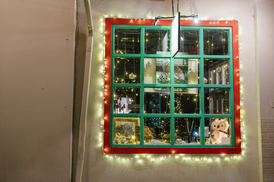 Owl figures, bird artwork, jewelry, and ornaments fill a colorful shop window in St. Augustine, Florida. Christmas lights frame the green and red window display at night.