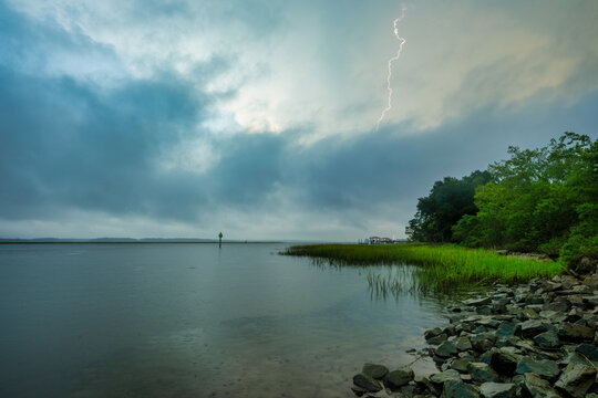 Dark clouds gather over the water as lightning strikes during a stormy evening by the shore
