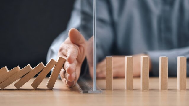 risk management governance. Hand stopping falling dominoes, symbolizing intervention and prevention of a chain reaction.