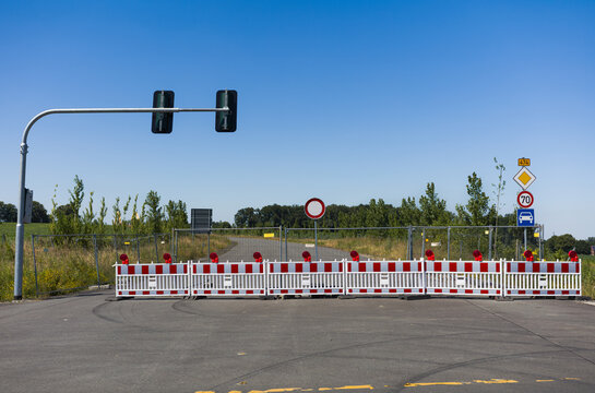 Road closed barricade with red and white construction barriers and traffic light under clear blue sky